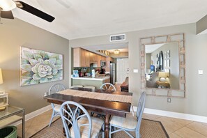 Un comedor con mesa y sillas de madera, una cocina al fondo y un espejo grande con marco decorativo.