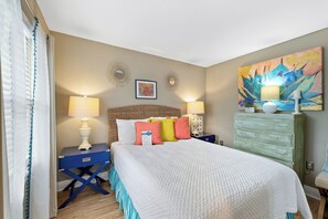 A hotel room with a large bed, two bedside tables with lamps, a decorative mirror, a wall painting, and a green dresser. - Surfside Shores 1803 by Liquid Life (Gulf Shores)