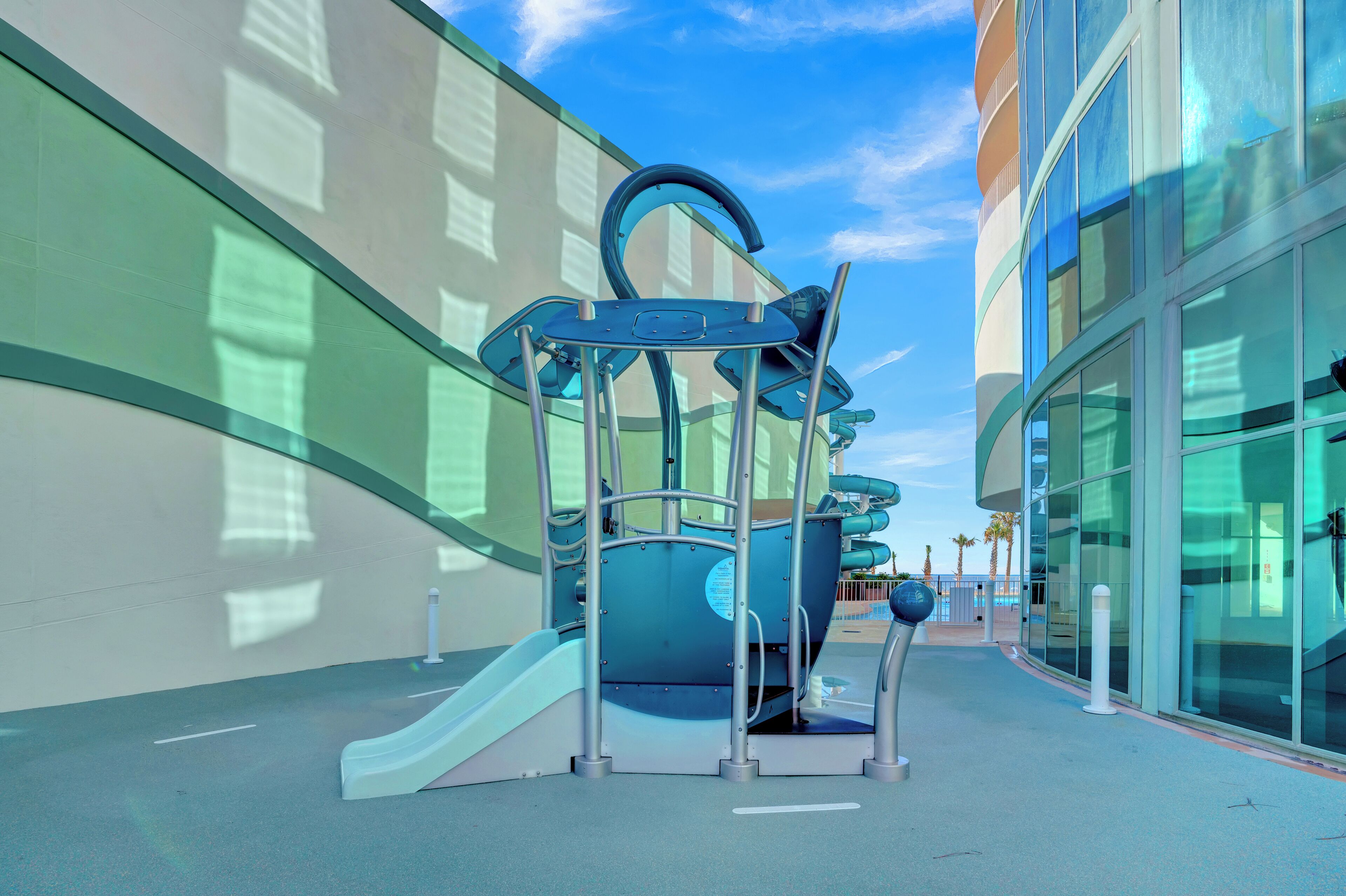 A playground structure with a slide and climbing elements, adjacent to a modern building with large windows.