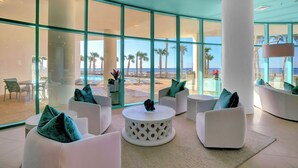 Uma área de estar moderna com mobiliário branco, janelas amplas e vista para a praia.