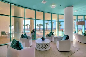 Ein moderner Lounge-Bereich mit weißen Möbeln, großen Fenstern und Blick auf den Strand.