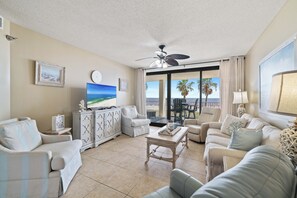 A spacious living room with a large flat-screen TV, comfortable seating, and a view of the ocean through a sliding glass door. - Windward Pointe 202 by Liquid Life (Orange Beach)