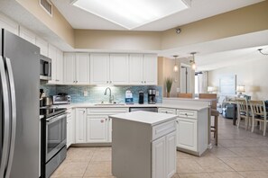 A modern kitchen with white cabinets, a central island, stainless steel appliances, and a blue-tiled backsplash. - Windward Pointe 202 by Liquid Life (Orange Beach)