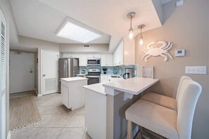 A modern kitchen with white cabinets, a central island, a microwave, and a refrigerator. - Windward Pointe 202 by Liquid Life (Orange Beach)