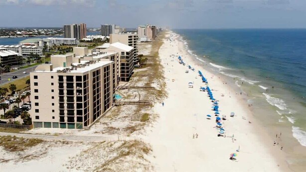 Un hotel frente a la playa con varios pisos, una playa de arena y vistas al océano.