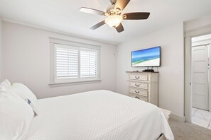 A bedroom with a bed, a ceiling fan, a television on a dresser, and a window with blinds. - Wind Drift 611SW by Liquid Life (Orange Beach)