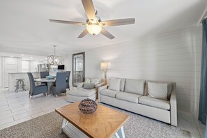 A modern living room with a ceiling fan, a dining area with a table and chairs, and a kitchen in the background. - Wind Drift 611SW by Liquid Life (Orange Beach)