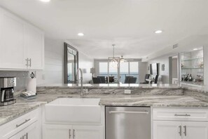 A modern kitchen with white cabinetry, a stainless steel sink, and a coffee maker. - Wind Drift 611SW by Liquid Life (Orange Beach)