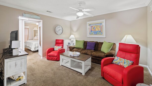 A living room with a ceiling fan, a sofa, two armchairs, a coffee table, a TV, and a lamp. - Beach Front 101 by Liquid Life (Gulf Shores)