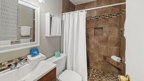 A bathroom with a sink, mirror, toilet, shower, and towel rack. - Beach Front 101 by Liquid Life (Gulf Shores)