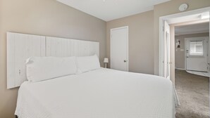 A bedroom with a large bed, a ceiling fan, a door, and a hallway leading to another room. - Beach Front 101 by Liquid Life (Gulf Shores)