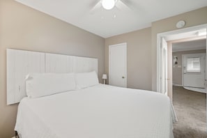 Ein Schlafzimmer mit einem großen Bett, einem Deckenventilator, einer Tür und einem Flur, der in einen anderen Raum führt.