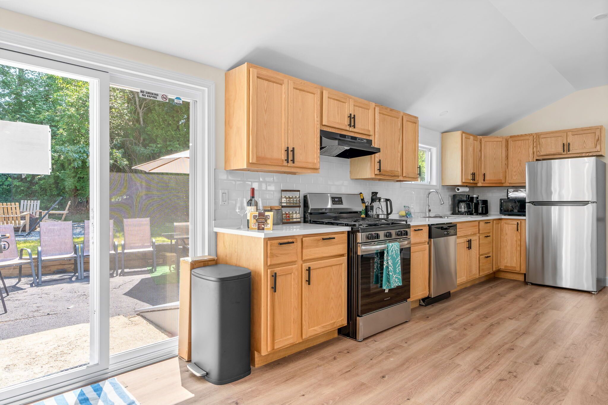 Una cocina moderna con armarios de madera, electrodomésticos de acero inoxidable y una puerta corrediza de vidrio que da a un espacio exterior.