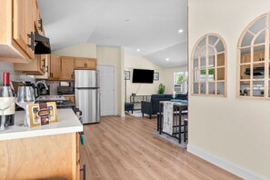 A modern kitchen with wooden cabinets, a stainless steel refrigerator, and a dining area with a table and chairs. - Lakeside Cape Cod Family Retreat, Fire Pit, BBQ and Nearby the beach! (Barnstable)