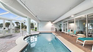 A swimming pool with a glass enclosure, surrounded by lounge chairs and a patio area. - Bel Sole 603 by Liquid Life (Gulf Shores)
