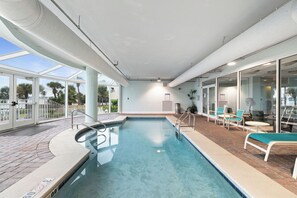 En swimmingpool med en glasvägg runt om, omgiven av solstolar och en uteplats.