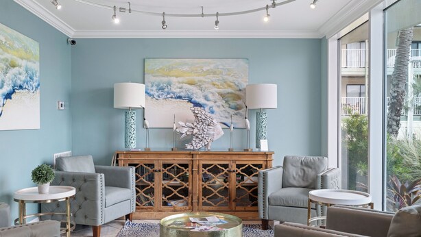 A modern living room with a large abstract painting, two armchairs, a coffee table, and a wooden cabinet with glass doors. - Bel Sole 603 by Liquid Life (Gulf Shores)