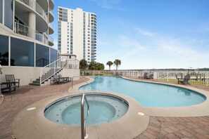 Une piscine avec un jacuzzi, des chaises longues et une vue sur un grand immeuble.