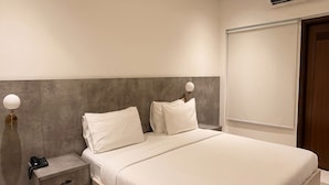 A modern bedroom with a large bed, bedside tables, a nightstand, and a wall-mounted air conditioning unit.