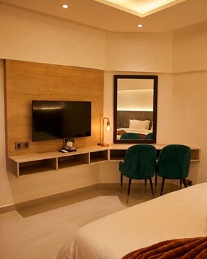 Ein Hotelzimmer mit Bett, Fernseher, Schreibtisch und zwei Stühlen sowie einem Spiegel.
