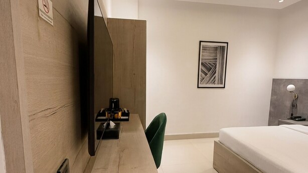 A modern bedroom with a wooden desk, a bed, a chair, and a flat-screen TV mounted on the wall.