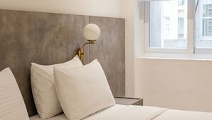 A hotel room with a bed, a nightstand, a lamp, and a window.