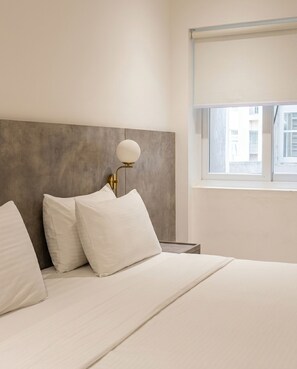 A hotel room with a bed, a nightstand, a lamp, and a window. - Hamsun Deluxe Double Room Clifton Karachi (Karachi)