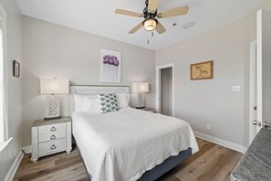 A bedroom with a bed, two bedside tables, a ceiling fan, and a door. - Bella Vista by Liquid Life (Gulf Shores)
