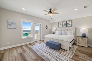 Ein Schlafzimmer mit einem großen Bett, einem Deckenventilator, Meerblick durch ein Fenster und einer Wanddekoration im Seestil.