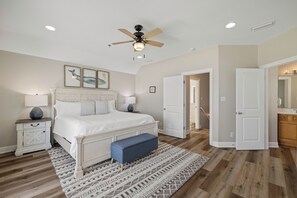 Ein Schlafzimmer mit Bett, Nachttischen, Deckenventilator und einer Tür zu einem anderen Raum.