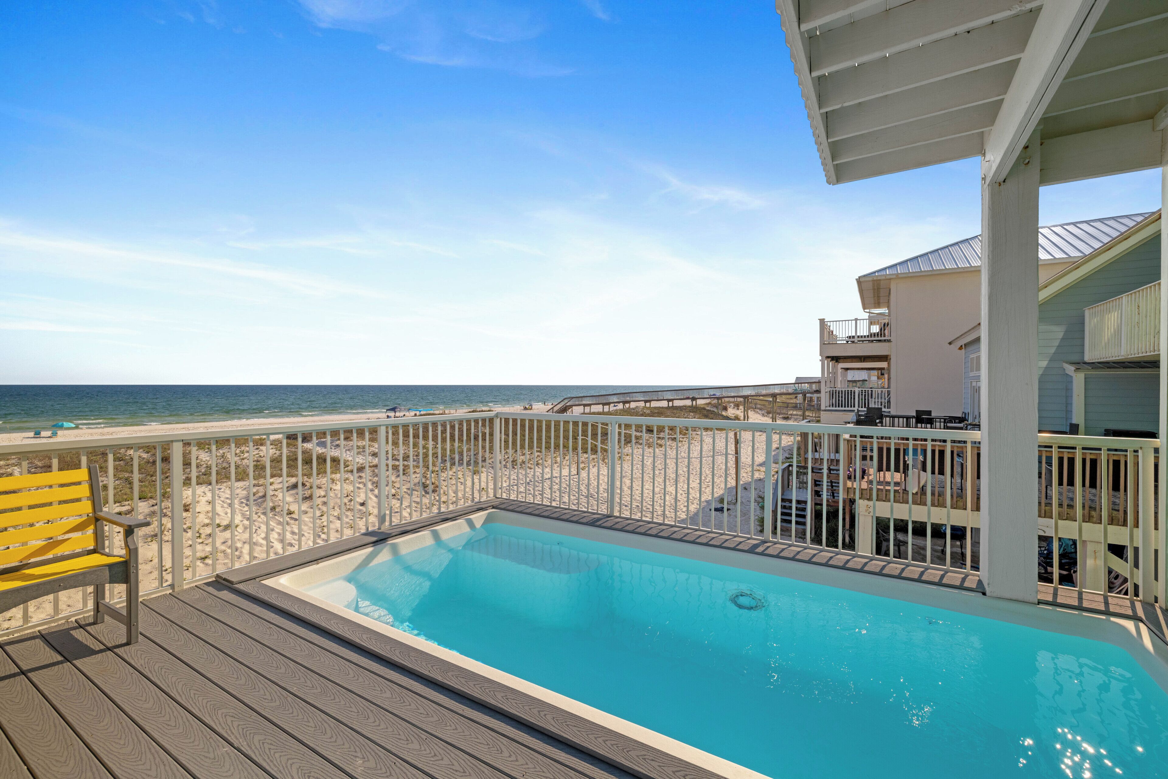 Zona de piscina con vista a la playa, muelle de madera y una silla amarilla.