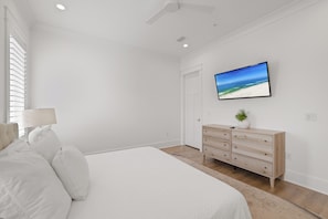 Een slaapkamer met een bed, een dressoir, een televisie aan de muur en een raam met zonwering.