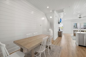 Een moderne keuken met witte kastjes, een houten eettafel en een ingebouwde televisie.