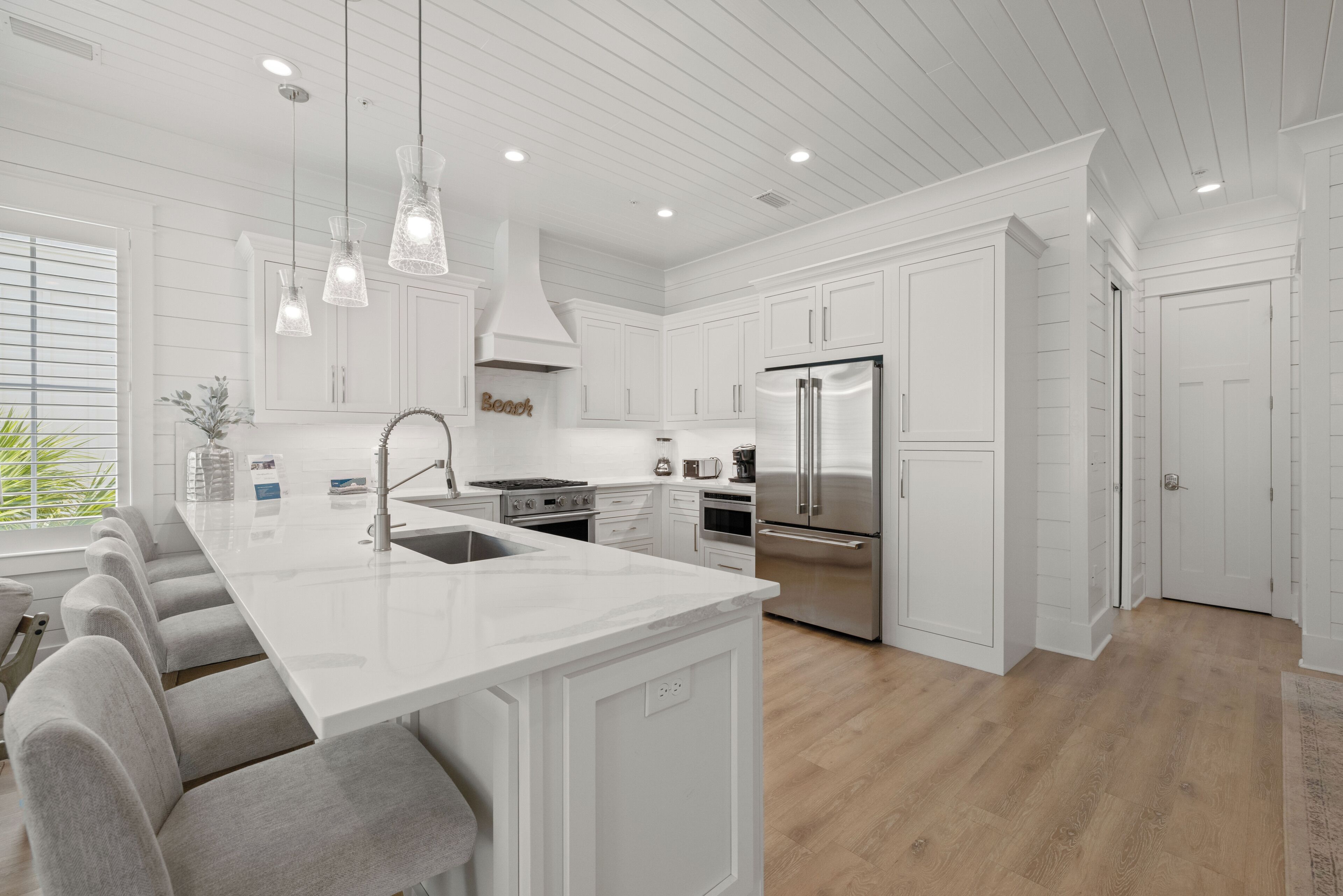 A modern kitchen with white cabinetry, stainless steel appliances, and a central island with bar stools.