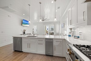A modern kitchen with white cabinetry, a central island, stainless steel appliances, and pendant lighting. - Bliss on the Bay by Liquid Life (Orange Beach)