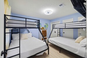 A bunk bed room with a ceiling fan, a wooden dresser, and a door. - Blissful Shores by Liquid Life (Gulf Shores)