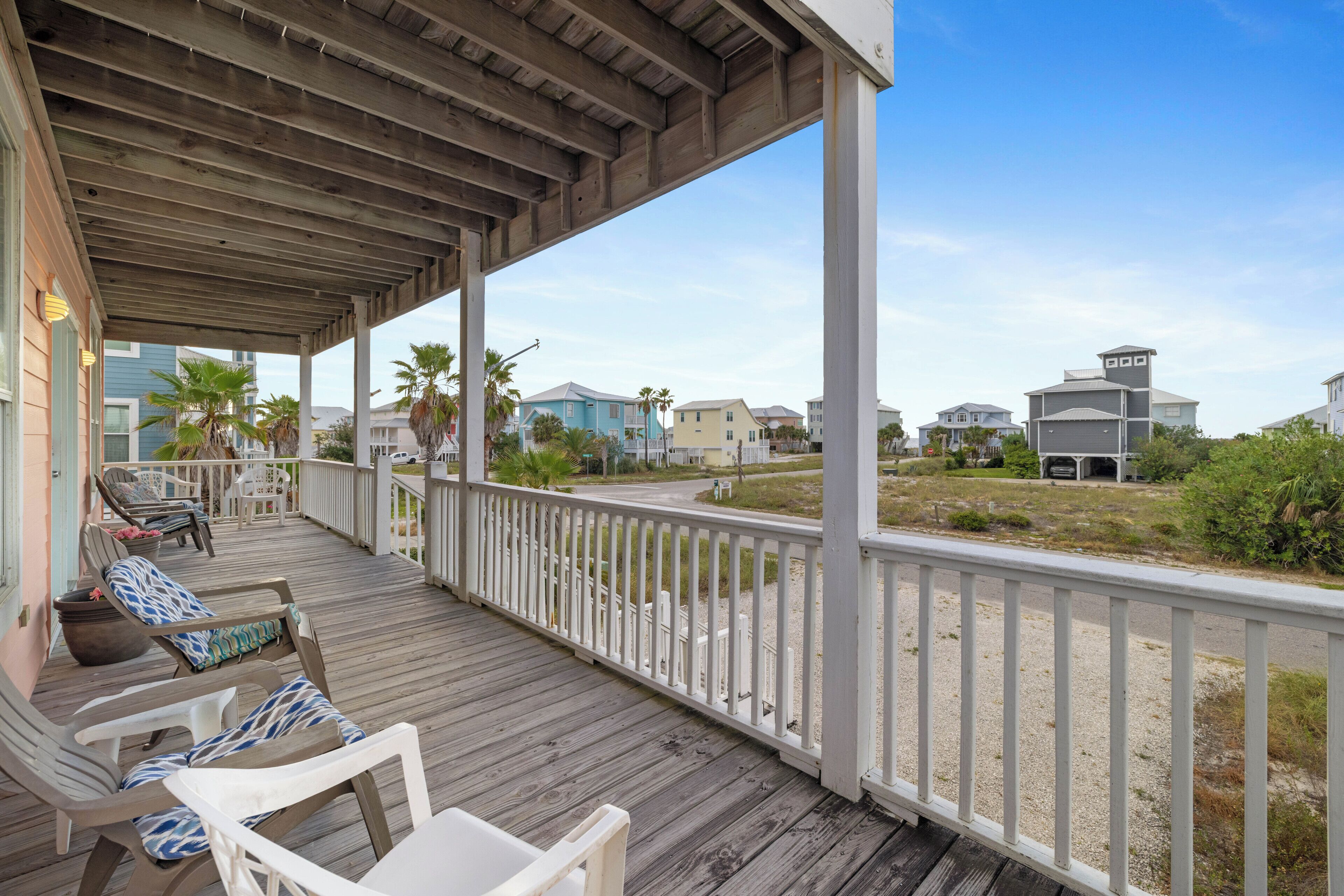 A covered outdoor area with a wooden deck, white railings, and several lounge chairs.