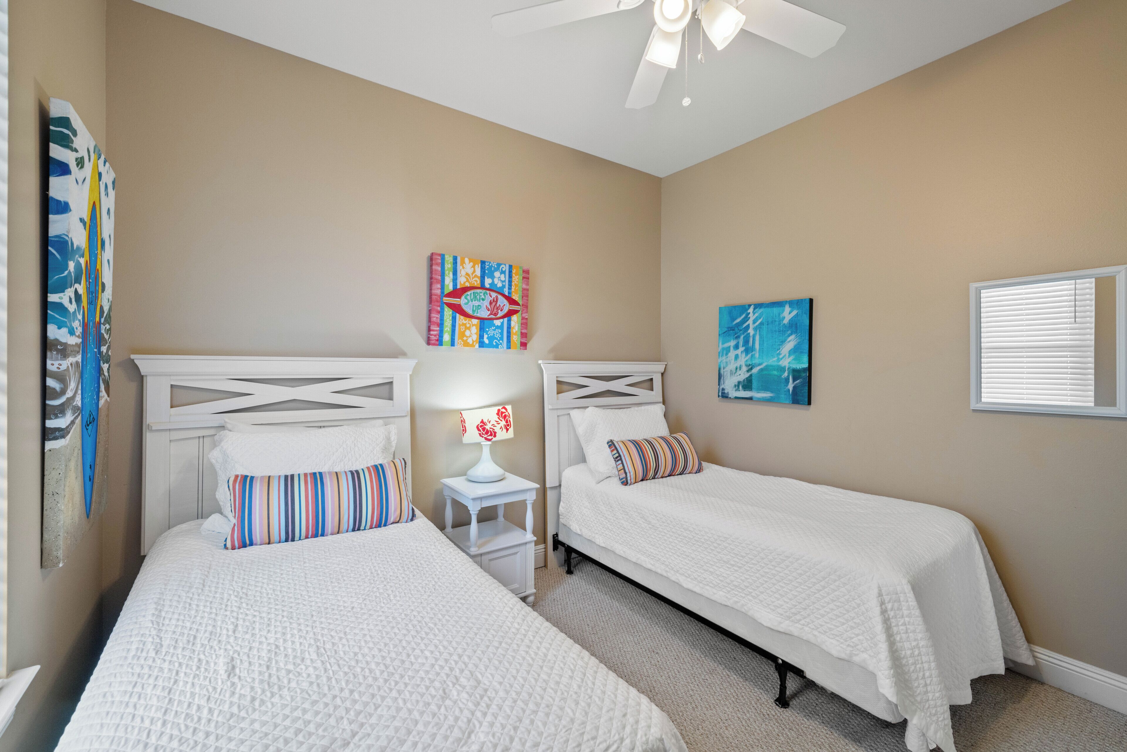 A bedroom with two beds, a ceiling fan, and artwork on the walls.