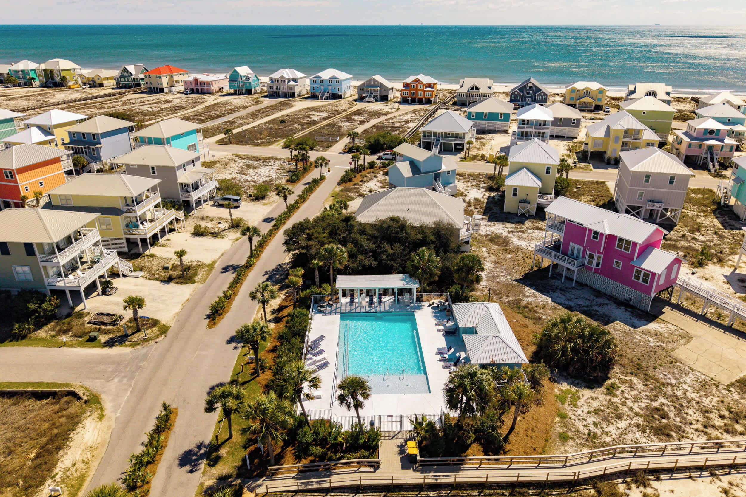 An aerial view of a coastal residential area with houses, a swimming pool, and a beach.
