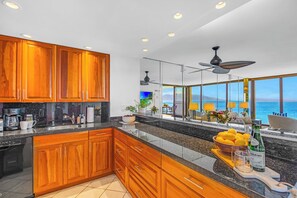 A modern kitchen with wooden cabinets, a granite countertop, and a view of the ocean. - Mahana Resort | Oceanfront Studio + 1 Bedroom Unit, Sleeps 6 | Car Incl. w/ 6+ Nights | ML-4139 (Lahaina)