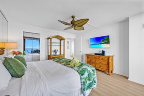 A hotel room with a bed, a wooden dresser, a television, a ceiling fan, and a large window with a view. - Mahana Resort | Oceanfront Studio + 1 Bedroom Unit, Sleeps 6 | Car Incl. w/ 6+ Nights | ML-4139 (Lahaina)