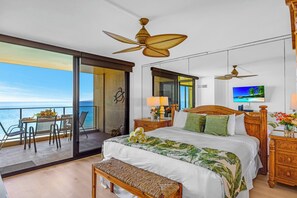 A bedroom with a large bed, a balcony with a table and chairs, a ceiling fan, and a TV. - Mahana Resort | Oceanfront Studio + 1 Bedroom Unit, Sleeps 6 | Car Incl. w/ 6+ Nights | ML-4139 (Lahaina)