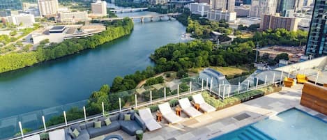 Piscina en la azotea con sillones de descanso, un horizonte urbano y un río.