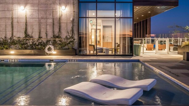 Una piscina amb gandules, un edifici modern amb grans finestres i vista a la zona de la piscina.