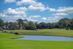 Ein Golfplatz mit Teich, Bäumen und einem Gebäude im Hintergrund.