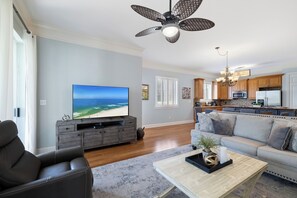 Ett modernt vardagsrum med en platt-TV, en grå TV-bänk, en lädersoffa, ett soffbord och en takfläkt.