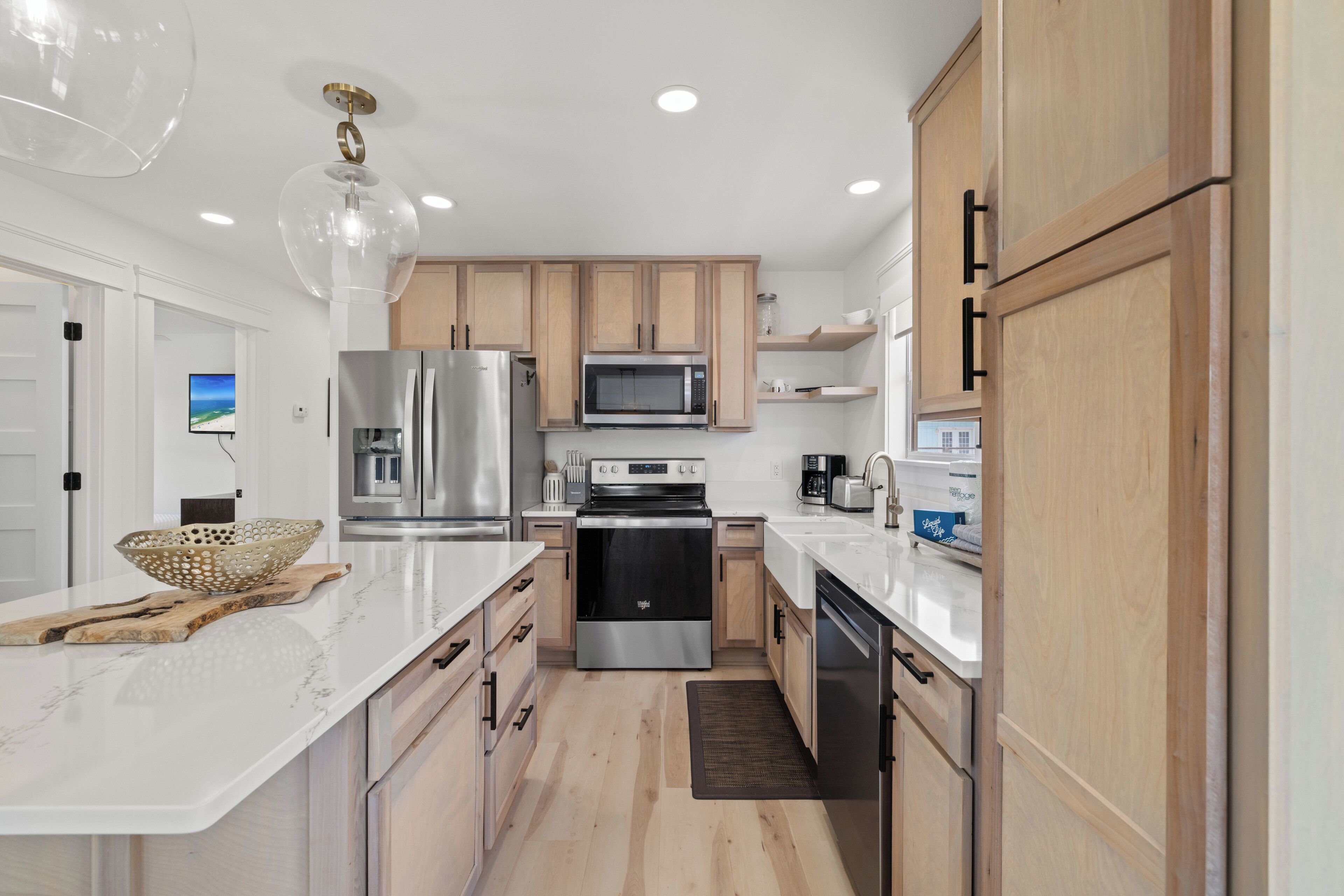 A modern kitchen with white countertops, stainless steel appliances, wooden cabinets, and a large island with a bowl.