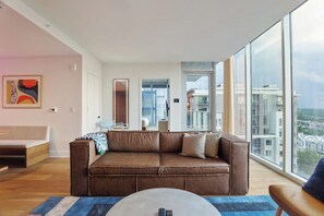 Ein modernes Wohnzimmer mit einem großen Fenster, einem braunen Ledersofa und einem blauen Teppich.