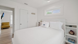 Een slaapkamer met een bed, een plafondventilator, een raam, een witte kast en een gele stoel.