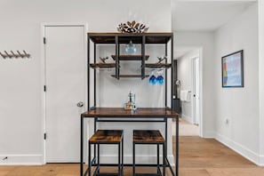 Ein Zimmer mit Holztisch, zwei Hocker, einem dekorativen Regal mit Gegenständen und einer Tür.